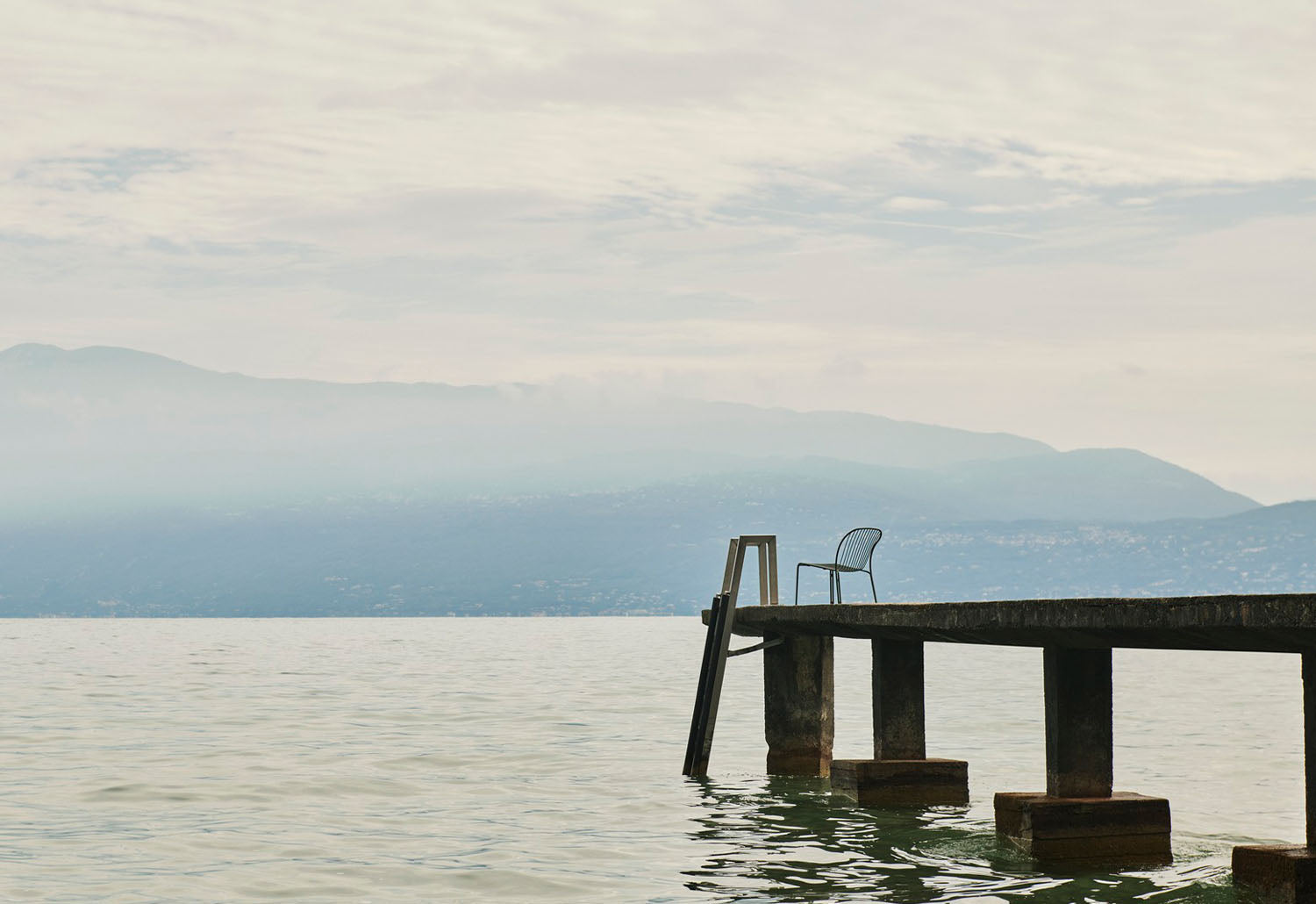  A single Thorvald Lounge Side Chair on a pier. The seat is designed by Space Copenhagen for &tradition in bronze green.